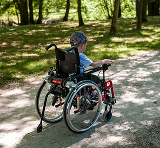 Enfant qui se promène dans un parc en fauteuil roulant avec une motorisation Mini Minotor 2.1de Benoit Systemes.
